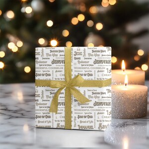 May include: A wrapped gift with a gold ribbon and bow, featuring religious text on the wrapping paper. Two lit candles with silver glitter are in the background, with bokeh lights. The gift is on a marble surface.
