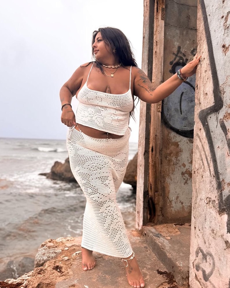May include: A white crochet top and matching skirt with a delicate floral pattern. The top has thin straps and a scoop neck. The skirt is long and flowing.