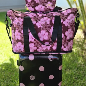 May include: A black Minnie Mouse rolling suitcase with pink polka dots, topped with a large dark brown travel bag featuring a pink hibiscus floral pattern and a matching small cosmetic bag with a handle, labeled 808 Mapuana's Gifts.