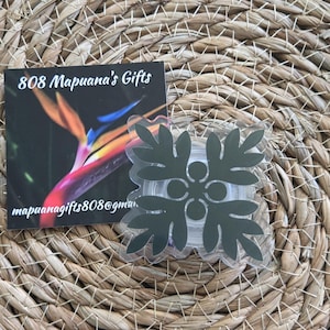 May include: A dark green Hawaiian flower design on a clear sticker. The sticker is on a woven brown surface. The text "808 Mapuana's Gifts" and "mapuanagifts808@gmail.com" are visible on a card behind the sticker.