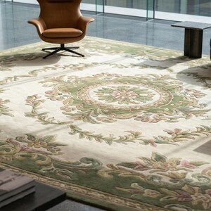 Puede incluir: Gran alfombra rectangular con fondo crema y un detallado dise&ntilde;o floral en tonos verdes y rosas. La alfombra presenta un dise&ntilde;o de medall&oacute;n central y un borde decorativo. Se encuentra en un espacio de vida moderno con sillones de cuero y un sof&aacute; oscuro. Mide aprox. 300 x 400 cm.
