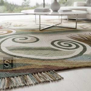 Puede incluir: Una alfombra hecha a mano con un dise&ntilde;o costero. La alfombra presenta un fondo crema con remolinos y rayas verdes, marrones y azules. La alfombra tiene un borde con flecos y est&aacute; colocada sobre un suelo de madera clara.