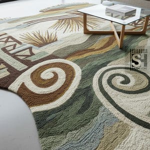 Puede incluir: Una alfombra grande y texturizada con un dise&ntilde;o abstracto. Presenta patrones arremolinados y formas geom&eacute;tricas en tonos marr&oacute;n, verde, beige y azul. La alfombra est&aacute; colocada sobre un suelo claro, con una mesa de centro con tapa de cristal al fondo.