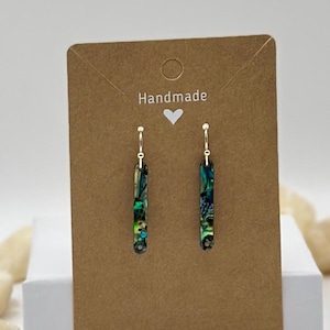 May include: A pair of handmade earrings with a rectangular shape and a colorful, iridescent design. The earrings are suspended from gold-colored hooks and are displayed on a brown card with the word "Handmade" and a heart symbol.