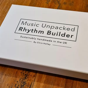 May include: White box with black text that reads "Music Unpacked Rhythm Builder" and "Sustainably handmade in the UK by Chris Holley".