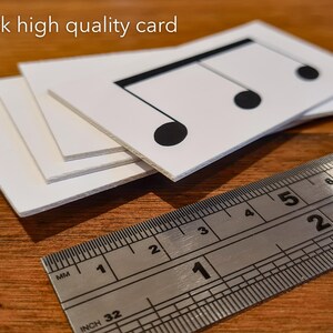 May include: Close-up of three thick, white cards stacked on top of each other. The top card has a black musical note printed on it. A ruler is placed below the cards, showing measurements in inches and millimetres.