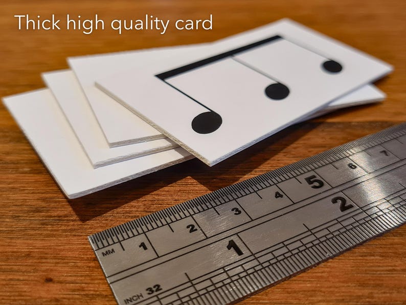 May include: Close-up of three thick, white cards stacked on top of each other. The top card has a black musical note printed on it. A ruler is placed below the cards, showing measurements in inches and millimetres.