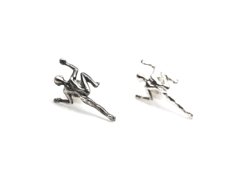 May include: A pair of silver earrings featuring a stylized human figure in a climbing pose.