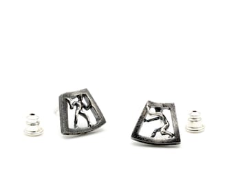 May include: A pair of silver earrings with a geometric design featuring a stylized figure inside each earring.