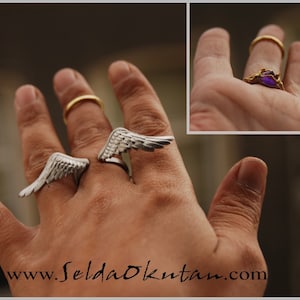 May include: Silver-toned wing rings and a gold ring are displayed on a hand. One wing ring is open, and the other is closed. A gold ring with a purple gemstone is also shown. The website address www.SeldaOkutan.com is visible.