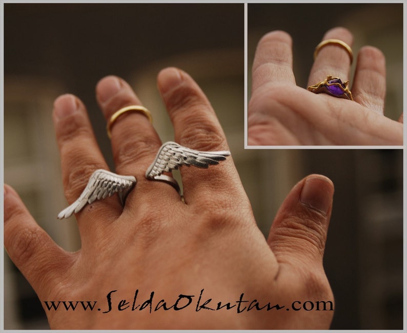 May include: Silver-toned wing rings and a gold ring are displayed on a hand. One wing ring is open, and the other is closed. A gold ring with a purple gemstone is also shown. The website address www.SeldaOkutan.com is visible.