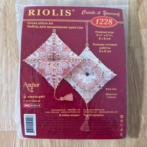 May include: A RIOLIS cross stitch kit in a clear plastic package. The kit features two diamond-shaped designs with intricate red and white patterns. The finished size is 3 1/4" x 3 1/4" (8 x 8 cm). The kit includes the Anchor and Zweigart brands.