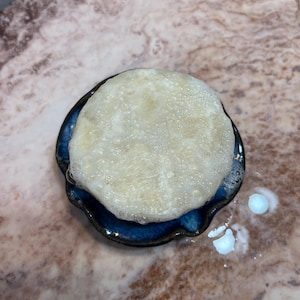 May include: A white, foamy soap bar in a blue and white ceramic dish. The soap is sitting on a light brown marble surface.