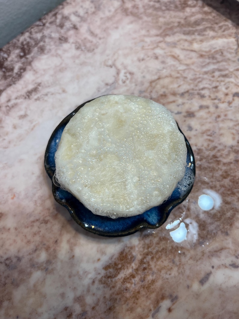 May include: A white, foamy soap bar in a blue and white ceramic dish. The soap is sitting on a light brown marble surface.