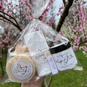 May include: A clear plastic bag filled with natural beauty products. The products include a bar of soap labeled "Roosterman Homestead", a deodorant stick labeled "All Natural Deodorant", a lip balm labeled "Honey Tallow Lip Balm", and a jar of whipped tallow labeled "All Natural Whipped Tallow".