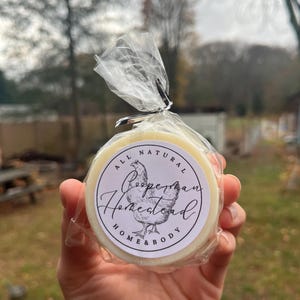 May include: A round, white soap bar with a white and black label that says "All Natural Cooperman Homestead Home & Body" with a chicken illustration.