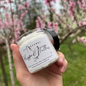 May include: A white jar with a black lid labeled "ALL NATURAL Whipped Tallow 4 oz" with the ingredients listed: "Grass-fed Suet Tallow, Organic Coconut Oil, Cold-pressed Hexane-free Castor Oil".