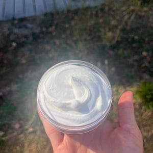 May include: A small clear container with a white, creamy substance inside. The substance is swirled and has a smooth, even texture.