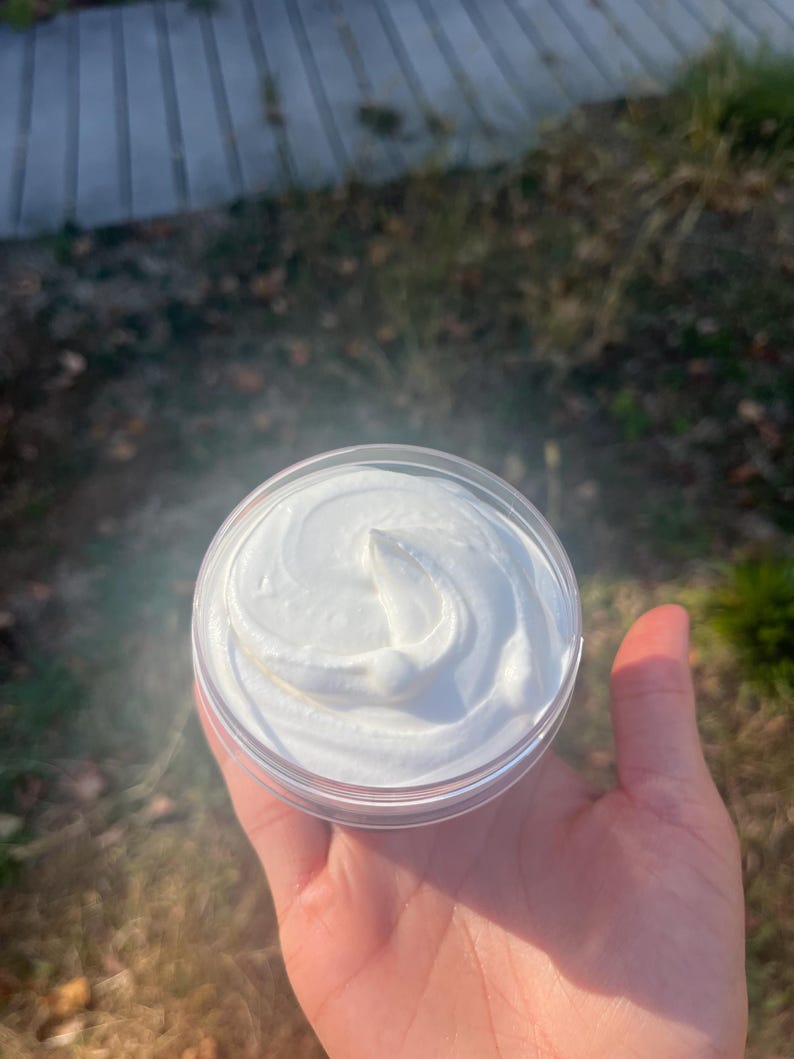 May include: A small clear container with a white, creamy substance inside. The substance is swirled and has a smooth, even texture.
