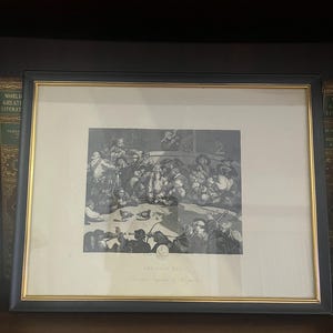May include: Framed black and gold print of a detailed, monochrome illustration depicting a crowded scene, likely from the 18th or 19th century. The print, titled "The Cock Pit," shows numerous figures in a lively setting. The frame is rectangular.