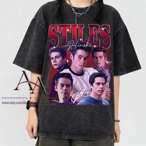 Könnte beinhalten: Dunkelgraues T-Shirt mit einem Grafikdesign, das mehrere Bilder einer Person, den Namen "STILES" in Rot und den Namen "Stilinski" darunter zeigt. Das T-Shirt hat einen Vintage-Look. Es ist ein Rundhalsausschnitt.