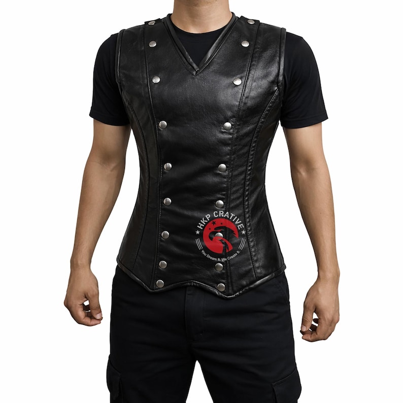 May include: Black leather vest with silver-colored buttons. The vest has a V-neck and a fitted design. The vest is worn over a black t-shirt. The vest has a logo on the lower right side.