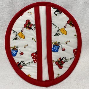 Puede incluir: Un agarrador de olla rojo y blanco con un diseño de pingüino navideño. El agarrador de olla tiene un borde rojo y un centro blanco con pingüinos, bastones de caramelo y calcetines.