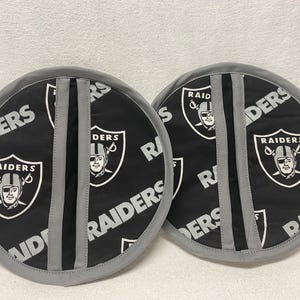 May include: Two gray and black fabric pot holders with the words "RAIDERS" and "RAID" printed on them. The pot holders have a black stripe down the center.