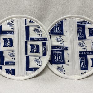 May include: Two white fabric pot holders with blue and white Duke University logos and text. The text includes "Blue Devils", "Duke", and "Home of the Blue Devils".