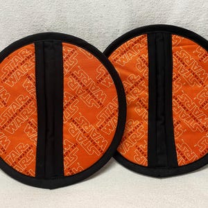 May include: Two orange and black round pot holders with the text "Star Wars" repeated in a circular pattern.