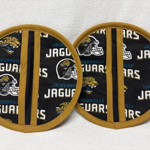 May include: Two round pot holders featuring the Jacksonville Jaguars logo and helmet design. The pot holders have a black background with gold and teal accents, and a gold trim. The text "Jaguars" is visible.