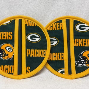 May include: Two green and yellow round pot holders with the Green Bay Packers logo and the words "Packers" and "G" on them.