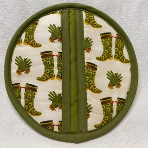 Può includere: Presa pentola verde e bianca con un design di stivali di gomma verdi e guanti da giardinaggio verdi. La presa pentola ha un bordo in tessuto verde.