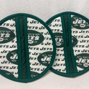 May include: Two green and white pot holders with the New York Jets logo and the words "Jets" repeated on them.