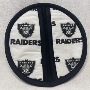 May include: Black and white pot holder with the Las Vegas Raiders logo repeated on a white background. The pot holder has a black border and a black fabric center.