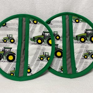 May include: Two green and white pot holders with a tractor pattern. The pot holders have a gray stripe down the center.