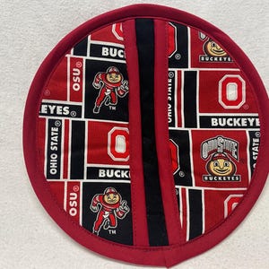 May include: Red and black fabric pot holder with a repeating pattern of the Ohio State Buckeyes logo, the word "Buckeyes", and the letter "O".