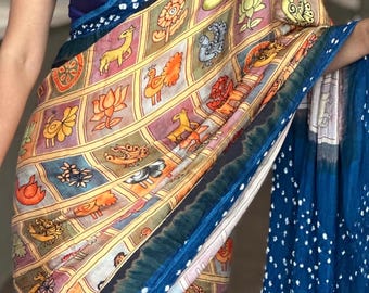 May include: A saree featuring a grid pattern with individual squares containing illustrations of animals, birds, and flowers in shades of orange, yellow, and grey. The garment includes a deep blue border with white dots and a solid dark blue blouse.