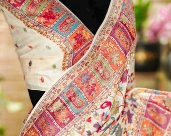 May include: Ivory saree with intricate floral and paisley patterns in a variety of colors, including red, orange, blue, and purple. The border features a detailed geometric design. The saree is draped over a black form.