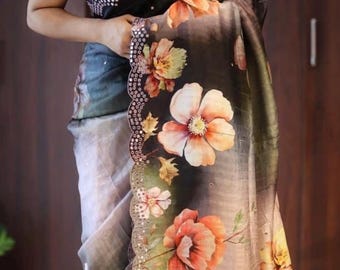 May include: A floral print saree with a black blouse. The saree features large, peach-colored flowers with green and yellow accents against a dark background. The border is embellished with small, silver-colored details.