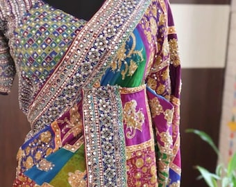 May include: A multi-colored saree featuring a patchwork design of purple, blue, green, and gold fabric panels. The garment is heavily embellished with intricate gold embroidery, sequins, and small reflective mirrors along the borders and bodice.
