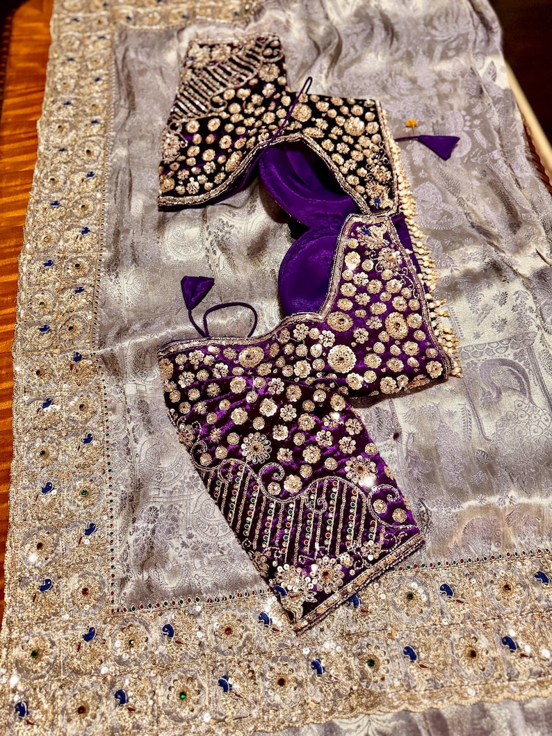 May include: A luxurious ensemble featuring a silver-gray fabric with intricate patterns and gold embellishments. Two ornate, velvet blouses in deep purple and black are adorned with gold sequins and embroidery. A traditional, elegant design.