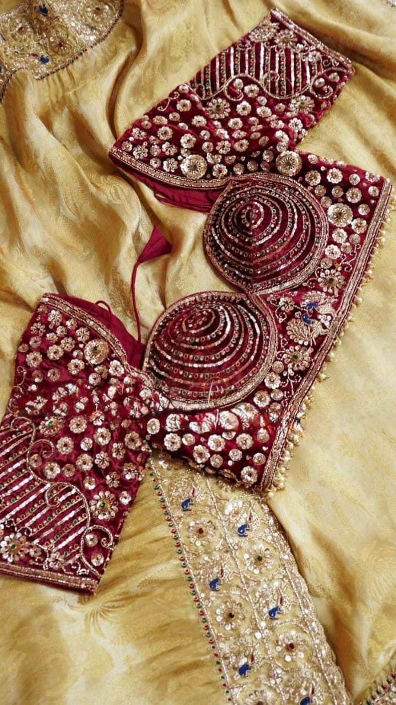 May include: A detailed shot of a maroon and gold embellished bodice and matching top. The garments are heavily decorated with sequins, beads, and embroidery. The background is a golden-yellow fabric, creating a luxurious feel.