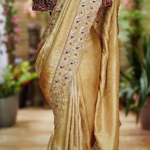May include: A golden-yellow sari with intricate embroidery and embellishments. The sari features a detailed border with blue and red accents. The blouse is a deep burgundy color with ornate detailing. The garment is draped over a mannequin.