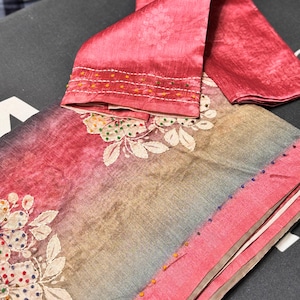 May include: A folded fabric piece featuring a gradient from deep pink to muted blue-gray. The textile is adorned with white floral embroidery accented by small, multicolored beads. A matching pink fabric strip with white stitching and beads is included.