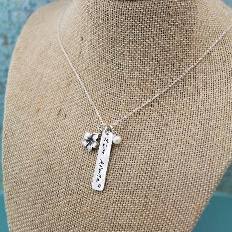 May include: A silver necklace with a charm that says "'ti'e Aloha" and a small flower charm and a pearl charm.