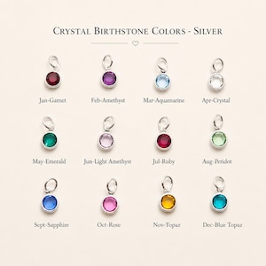 May include: A chart titled Crystal Birthstone Colors - Silver displaying twelve circular silver charms with colored crystals. Each charm is labeled with a month and gemstone name: Jan-Garnet, Feb-Amethyst, Mar-Aquamarine, Apr-Crystal, May-Emerald, Jun-Light Amethyst, Jul-Ruby, Aug-Peridot, Sept-Sapphire, Oct-Rose, Nov-Topaz, and Dec-Blue Topaz.