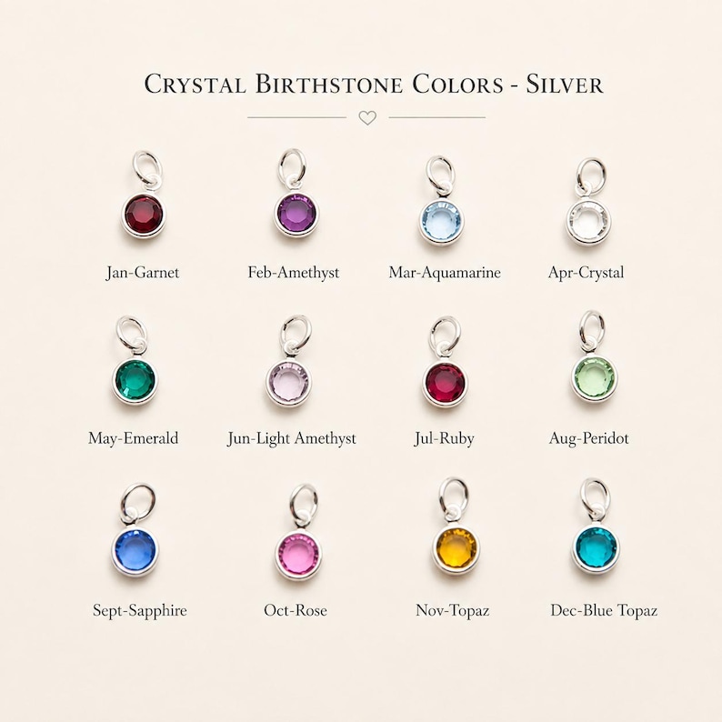 May include: A chart titled Crystal Birthstone Colors - Silver displaying twelve circular silver charms with colored crystals. Each charm is labeled with a month and gemstone name: Jan-Garnet, Feb-Amethyst, Mar-Aquamarine, Apr-Crystal, May-Emerald, Jun-Light Amethyst, Jul-Ruby, Aug-Peridot, Sept-Sapphire, Oct-Rose, Nov-Topaz, and Dec-Blue Topaz.