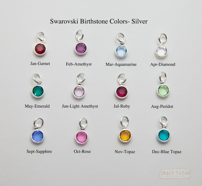 May include: Twelve silver charms with different colored Swarovski birthstones. Each charm is labeled with the month and birthstone name. The birthstones are: Garnet, Amethyst, Aquamarine, Diamond, Emerald, Light Amethyst, Ruby, Peridot, Sapphire, Rose, Topaz, and Blue Topaz.