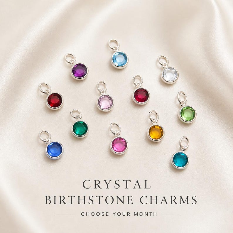 May include: A collection of twelve circular silver charms, each featuring a different colored crystal birthstone. The charms are arranged in a scattered pattern. Below the charms, the text reads: CRYSTAL BIRTHSTONE CHARMS CHOOSE YOUR MONTH.